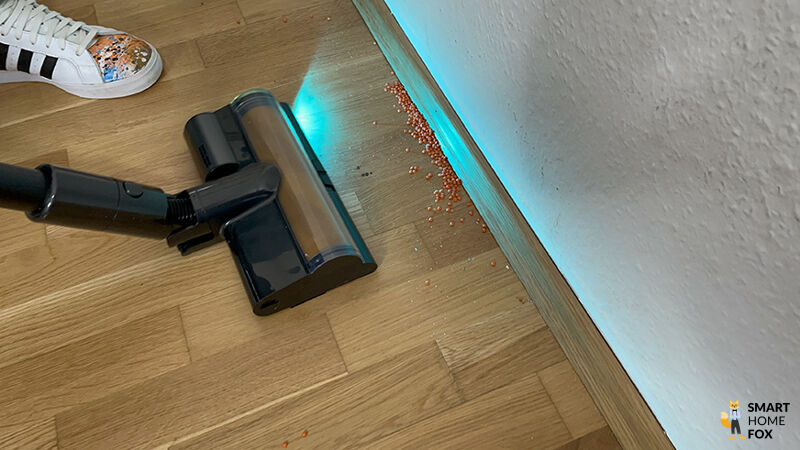 Die Dreame Z40 Station bei der Randreinigung entlang einer Sockelleiste mit aktiver Blaulichtausleuchtung.